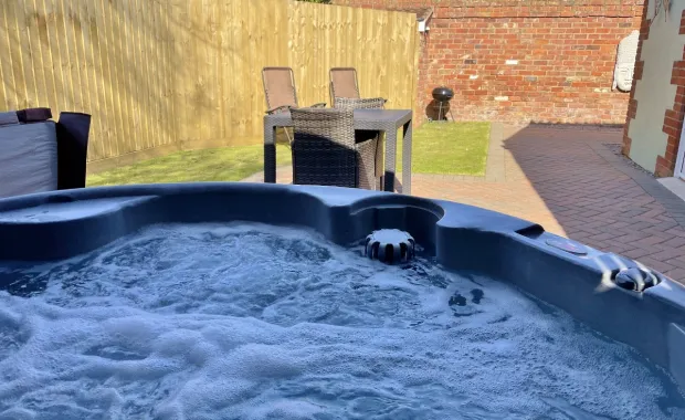 Holly Cottage's private courtyard at Mill Farm Leisure featuring a bubbling hot tub, outdoor seating, and a block paved patio.