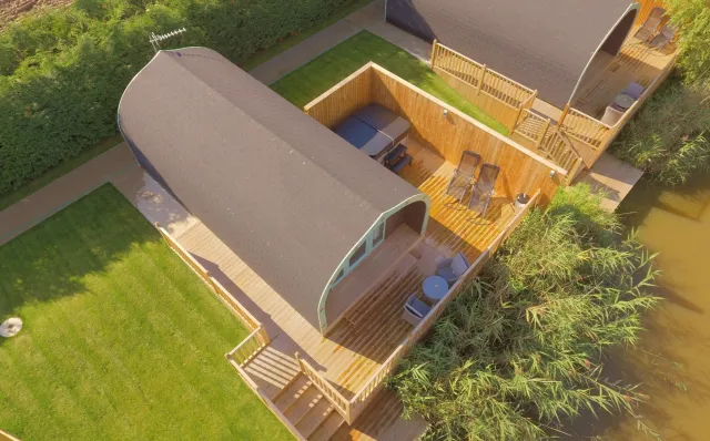 Beech Lodge at Mill Farm Leisure, aerial view showcasing its wooden deck with outdoor furniture, Hot tub and proximity to the lake surrounded by greenery.