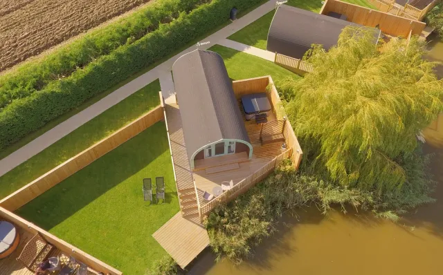 Oak Lodge aerial view with decking, seating, hot tub, dog-friendly garden and adjacent lake.